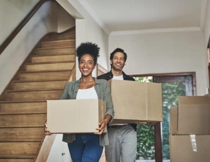 A couple carrying moving boxes into their new home.